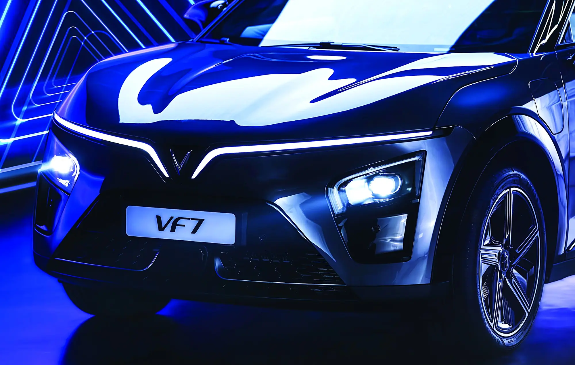 The glowing V-shaped light bar on the front of a VinFast VF 7 at night