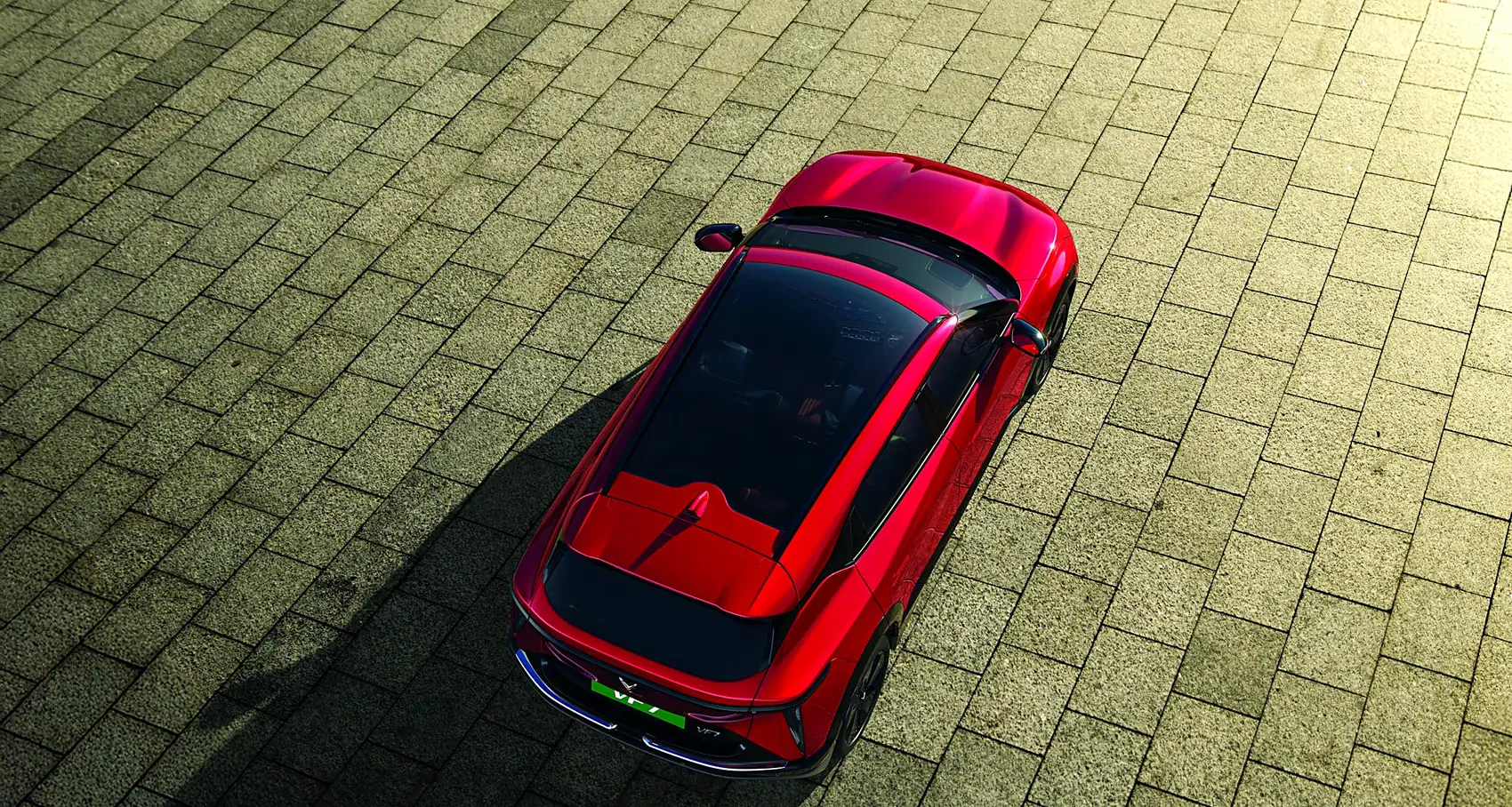 A red VinFast VF 7 seen from above on cobblestones, with its long shadow